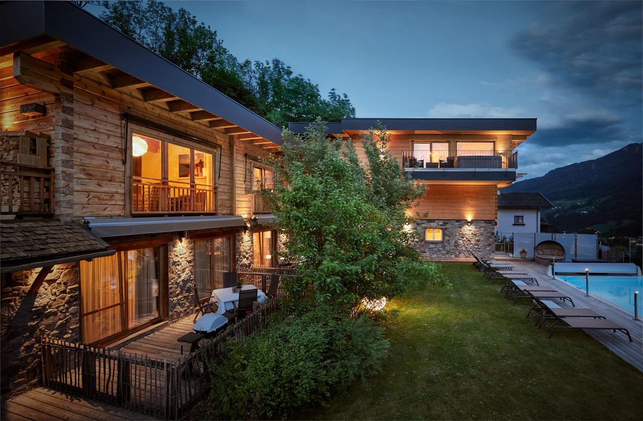 Beleuchtete Holzapartments Sonnenhang mit Garten und Pool am Abend
