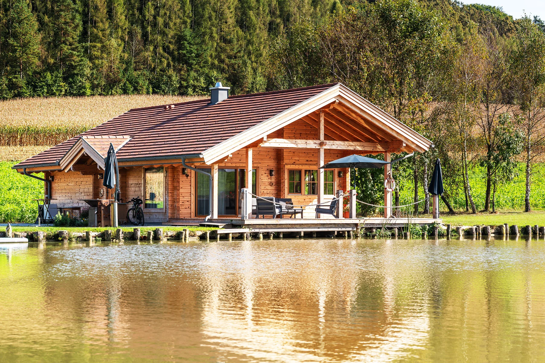 Ein Holzhaus mit sonniger Terrasse und ruhigem Teich, umgeben von Natur